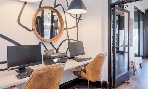 Business center at Reatta Ranch apartments in Justin, TX with two computers, printer, leather chairs, mirror, and wall art