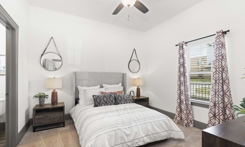 Apartment bedroom with upholstered headboard, ceiling fan, and balcony window