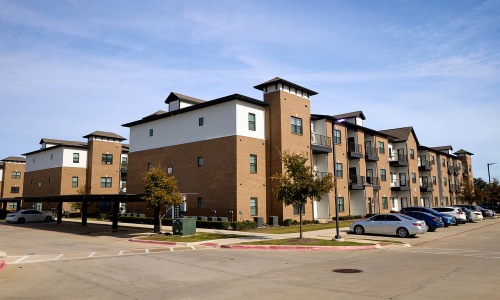 Four-story brick apartment buildings with covered carports at Reatta Ranch Justin TX