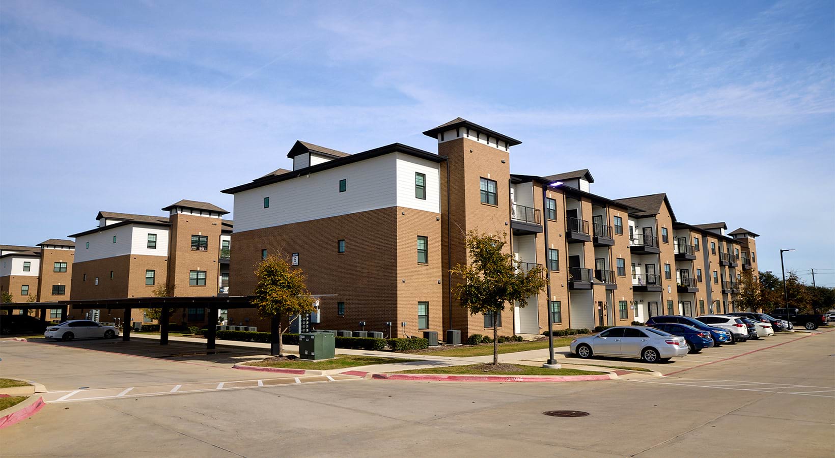Four-story brick apartment buildings with covered carports at Reatta Ranch Justin TX